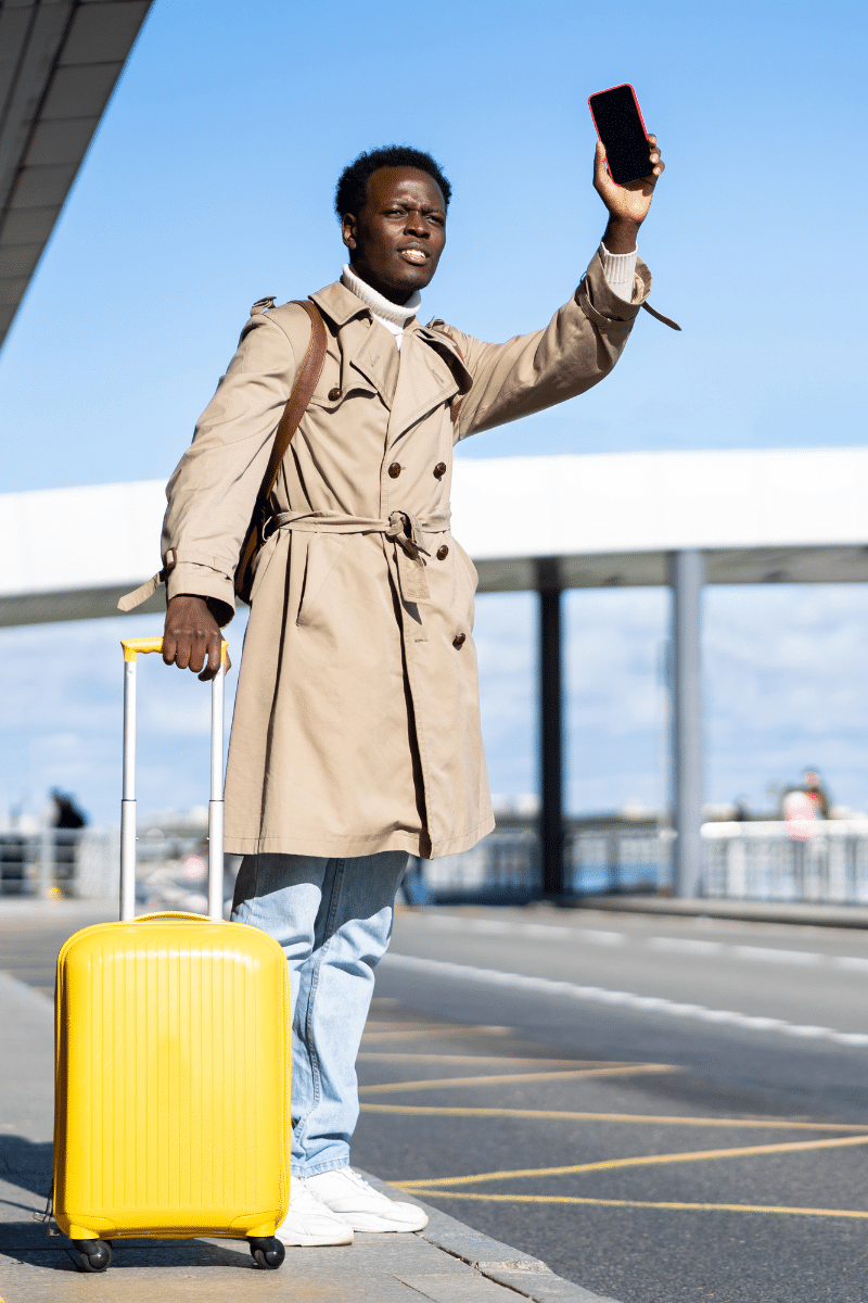 un monsieur entrain de lever le bras pour appeler un taxi devant un aéroport